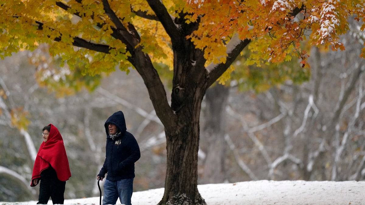 People walk past a glowing tree as they visit a park during the first snow of the season Monday, Oct. 26, 2020, in Merriam, Kan.