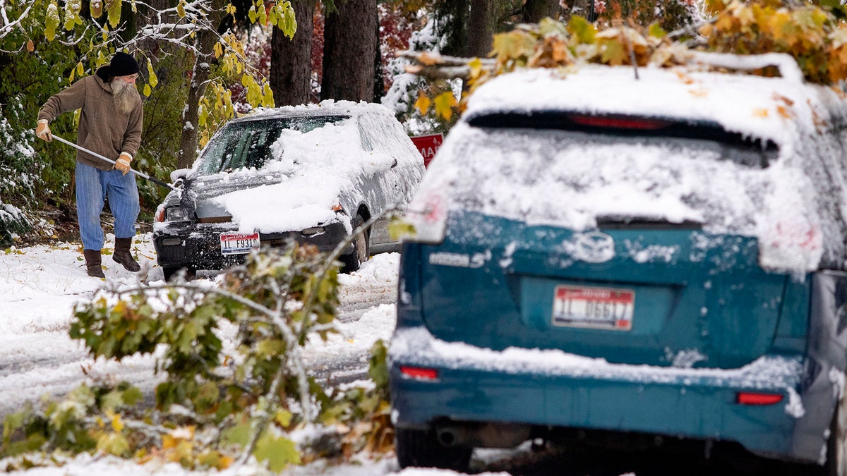 Tim Daulton clears snow off of his car across the street from a car with small tree branches on it on Saturday, Oct. 24, 2020, in Moscow, Idaho.
