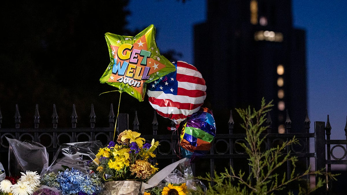 Flowers and balloons left by supporters of President Donald Trump at the entrance to Walter Reed National Military Medical Center (background) in Bethesda, Md., Sunday, Oct. 4, 2020. Trump was admitted to the hospital after contracting the coronavirus. (AP Photo/Cliff Owen)