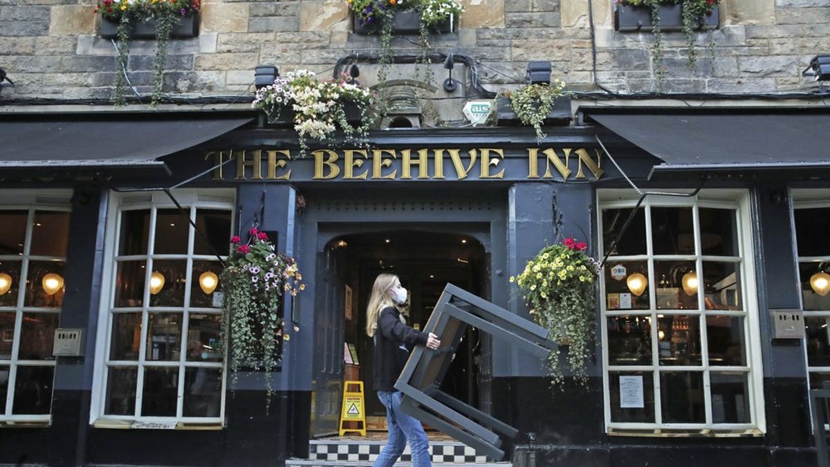 A worker removes tables from outside the Beehive Inn, as temporary restrictions announced by First Minister Nicola Sturgeon to help curb the spread of coronavirus have come into effect at 6 p.m. Friday in Edinburgh. (Andrew Milligan/PA via AP)
