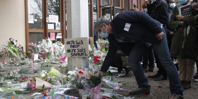 A man lays a flower outside the school where a slain history teacher was working, Saturday, Oct. 17, 2020, in Conflans-Sainte-Honorine, northwest of Paris. French President Emmanuel Macron denounced what he called an "Islamist terrorist attack" against a history teacher decapitated in a Paris suburb Friday, urging the nation to stand united against extremism. The teacher had discussed caricatures of Islam's Prophet Muhammad with his class, authorities said. The suspected attacker was shot to death by police after Friday's beheading. (AP Photo/Michel Euler)