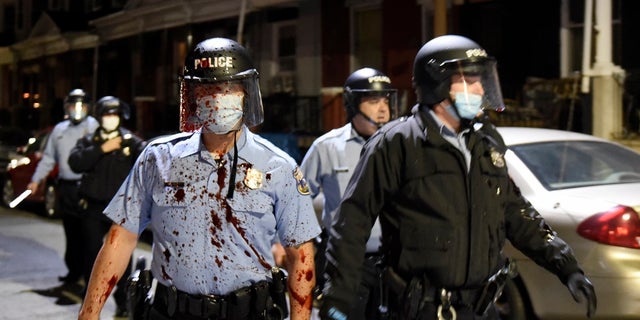 A Philadelphia police officer is covered with an unidentified red substance during a confrontation with protesters, Tuesday, Oct. 27, 2020, in Philadelphia. (AP Photo/Michael Perez)