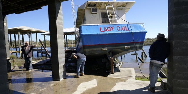 Boat owner Ricky Mitchell, center, and his friend Buck, left, no last name given, survey damage to his boat that washed up against the home of Ray Garcia, in Lakeshore, Miss., Thursday, Oct. 29, 2020. Hurricane Zeta passed through Wednesday with a tidal surge that caused the boat to become unmoored. (AP Photo/Gerald Herbert)