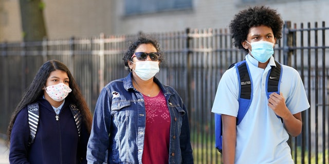 A mother accompanies her children as they arrive for the first day of in-person classes at Erasmus High School in Brooklyn's Flatbush neighborhood, Thursday, Oct. 1, 2020 in New York. The city's plans to send kids back into classrooms rely on an ambitious plan to do random virus testing of pupils and staff throughout the school year. (AP Photo/Mark Lennihan)