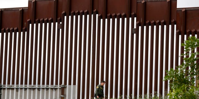 FILE - In this March 18, 2020, file photo, a Border Patrol agent walks along a border wall separating Tijuana, Mexico, from San Diego, in San Diego. Vice President Mike Pence in March directed the nation’s top disease control agency to use its emergency powers to effectively seal the U.S. borders, overruling the agency’s scientists who said there was no evidence the action would slow the coronavirus, according to two former health officials. (AP Photo/Gregory Bull, File)