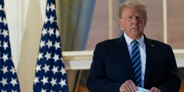 President Donald Trump removes his mask as he stands on the Blue Room Balcony upon returning to the White House Monday, Oct. 5, 2020, in Washington after leaving Walter Reed National Military Medical Center, in Bethesda, Md. (AP Photo/Alex Brandon)