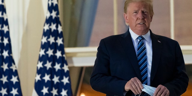 President Donald Trump removes his mask as he stands on the Blue Room Balcony upon returning to the White House Monday, Oct. 5, 2020, in Washington after leaving Walter Reed National Military Medical Center, in Bethesda, Md. (AP Photo/Alex Brandon)