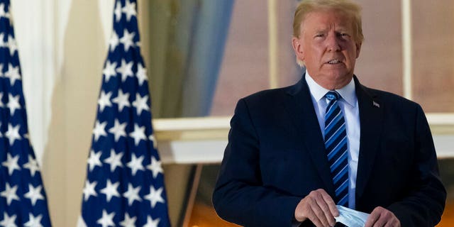 President Trump holds his face mask as he stands on the Blue Room Balcony upon returning to the White House Monday, Oct. 5, 2020, in Washington, after leaving Walter Reed National Military Medical Center, in Bethesda, Md. (AP Photo/Alex Brandon)