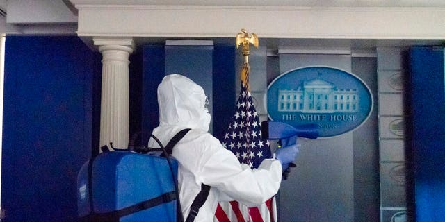 A member of the cleaning staff sprays the James Brady Briefing Room of the White House, Monday, Oct. 5, 2020, in Washington. (AP Photo/Alex Brandon)