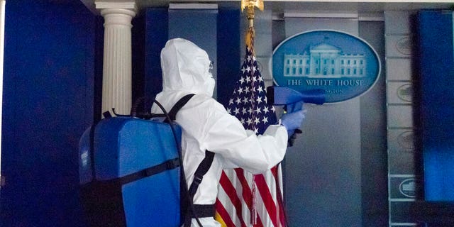 A member of the cleaning staff sprays the James Brady Briefing Room of the White House, Monday, Oct. 5, 2020, in Washington. (AP Photo/Alex Brandon)