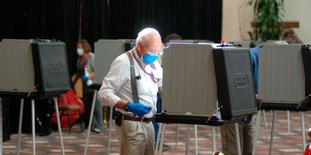Temporary election worker Joseph Banar disinfects voting stations as a precaution against the coronavirus, while a steady stream of voters participates in the first day of balloting in New Mexico at the Santa Fe Convention Center on Tuesday, Oct. 6, 2020. (AP Photo/Morgan Lee)