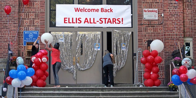 School staff help to decorate the front entrance of the Ellis Elementary School in Boston's Roxbury neighborhood before opening for the first day back of in person learning during the COVID-19 coronavirus pandemic, Thursday, Oct. 1, 2020. (David L Ryan/The Boston Globe via AP)