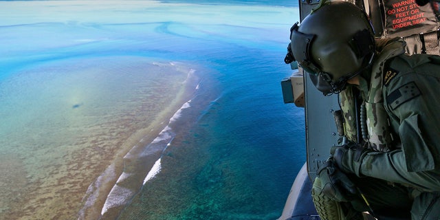 In this Sept. 25, 2020, photo provided by the Royal Australian Navy, Leading Seaman Daniel Atkins looks out over Elizabeth Reef in search of unexploded ordnance on an MRH-90 helicopter from HMAS Adelaide. The 45-kilogram (100-pound) bomb was found by a fisherman on Elizabeth Reef near Lord Howe Island, about 550 kilometers (340 miles) off New South Wales state. (Sgt. Jake Sims/Royal Australian Navy via AP)