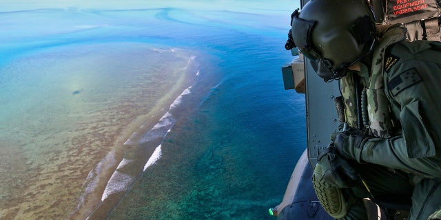 In this Sept. 25, 2020, photo provided by the Royal Australian Navy, Leading Seaman Daniel Atkins looks out over Elizabeth Reef in search of unexploded ordnance on an MRH-90 helicopter from HMAS Adelaide. The 45-kilogram (100-pound) bomb was found by a fisherman on Elizabeth Reef near Lord Howe Island, about 550 kilometers (340 miles) off New South Wales state. (Sgt. Jake Sims/Royal Australian Navy via AP)