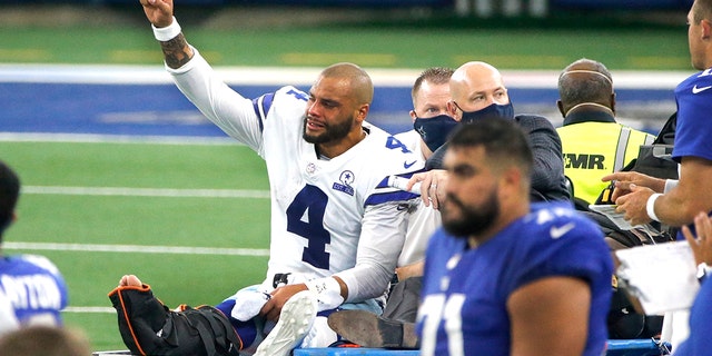 Dallas Cowboys quarterback Dak Prescott (4) lifts his fist to cheers from fans as he is carted off the field after suffering a lower right leg injury running the ball in the second half of an NFL football game against the New York Giants in Arlington, Texas, Sunday, Oct. 11, 2020. (AP Photo/Michael Ainsworth)