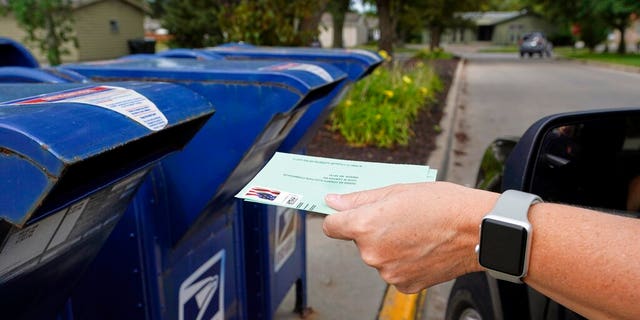 A person drops applications for mail-in-ballots into a mailbox in Omaha, Neb. (AP Photo/Nati Harnik, File)