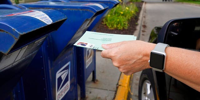 A person drops applications for mail-in-ballots into a mailbox in Omaha, Neb. (AP Photo/Nati Harnik, File)