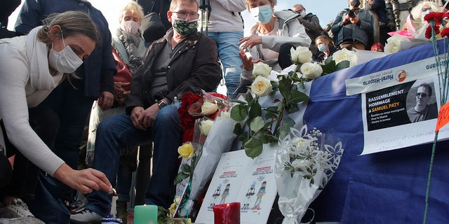 A woman lights a candle on Republique square during a demonstration Sunday Oct. 18, 2020 in Paris. (AP Photo/Michel Euler)