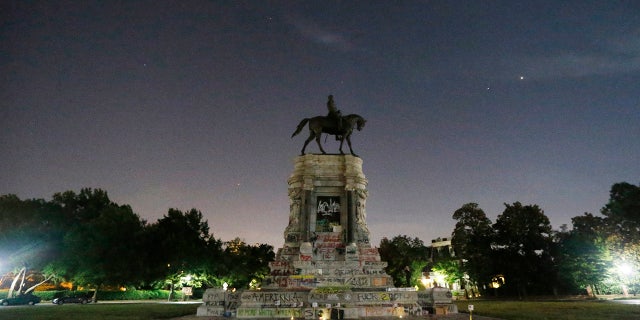 The moon and street lights illuminate the statue of Confederate General Robert E. Lee on Monument Avenue Friday June. 5, 2020, in Richmond, Va. A lawsuit seeking to prevent Virginia Gov. Ralph Northam from removing the statue is scheduled to go to trial Monday, Oct. 19, 2020. (AP Photo/Steve Helber)