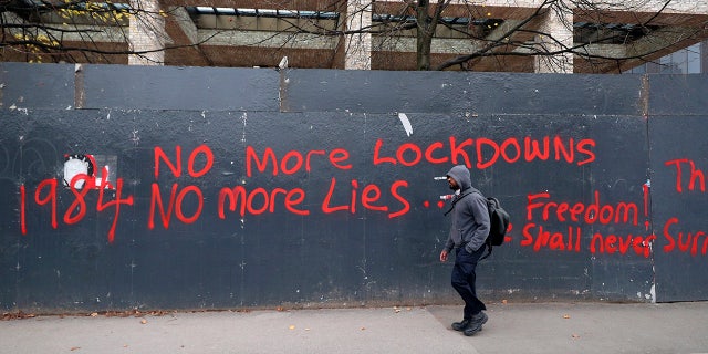A man walks past anti-lockdown graffiti in Manchester, England, Monday, Oct. 19, 2020 as the row over Greater Manchester region's coronavirus status continues. Britain’s government says discussions about implementing stricter restrictions in Greater Manchester must be completed Monday because the public health threat caused by rising COVID-19 infections is serious and getting worse. (Peter Byrne/PA via AP)