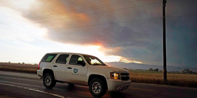 Smoke rises from mountain ridges as several wildfires burn in the state Wednesday, Oct. 21, 2020, as traffic moves along 75th street in Niwot, Colo. (Associated Press)