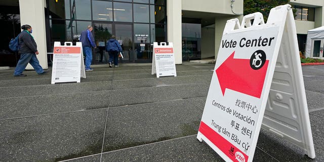 People walk near a sign at the King County election headquarters Oct. 23, 2020.