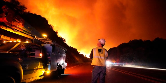 In this Tuesday, Sept. 8, 2020 file photo, A Pacific Gas and Electric worker looks up at the advancing Creek Fire along Highway 168 near Alder Springs, Calif. Pacific Gas & Electric will cut power to over 1 million people on Sunday to prevent the chance of sparking wildfires as extreme fire weather returns to the region, the utility announced Friday. Oct. 23, 2020. (AP Photo/Marcio Jose Sanchez, File)