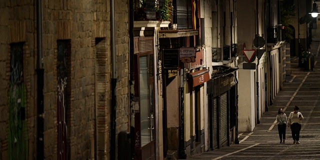 Residents wearing face mask protection as they walk along an empty Javier street, in Pamplona, northern Spain, Saturday, Oct. 24, 2020, as new measures against the coronavirus began in the Navarra province where all bar and restaurants are closed for 15 days from Wednesday midnight. (AP Photo/Alvaro Barrientos)