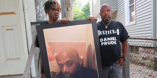 In this Sept. 3, 2020, file photo, Joe Prude, brother of Daniel Prude, right, and his son Armin, stand with a picture of Daniel Prude in Rochester, N.Y. (AP Photo/Ted Shaffre, File)