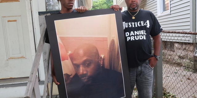In this Sept. 3, 2020, file photo, Joe Prude, brother of Daniel Prude, right, and his son Armin, stand with a picture of Daniel Prude in Rochester, N.Y. (AP Photo/Ted Shaffre, File)