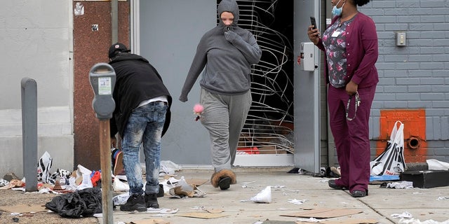 People walk out of a damaged store Tuesday in Philadelphia after a protest over the death of Walter Wallace, a Black man who was killed by police in Philadelphia. Police shot and killed the 27-year-old Monday on a Philadelphia street after yelling at him to drop his knife, sparking violent protests that police said injured 30 officers and led to dozens of arrests. (AP Photo/Michael Perez)