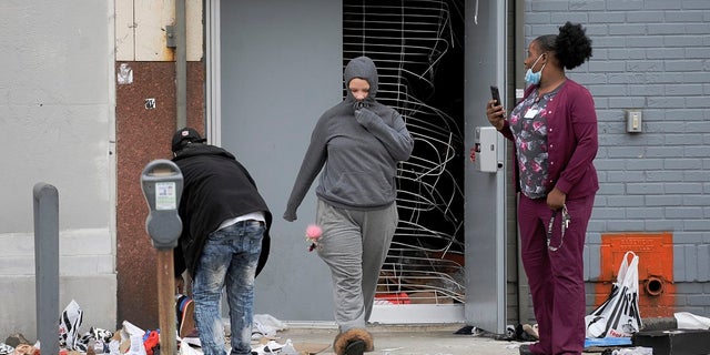 People walk out of a damaged store Tuesday in Philadelphia after a protest over the death of Walter Wallace, a Black man who was killed by police in Philadelphia. Police shot and killed the 27-year-old Monday on a Philadelphia street after yelling at him to drop his knife, sparking violent protests that police said injured 30 officers and led to dozens of arrests. (AP Photo/Michael Perez)