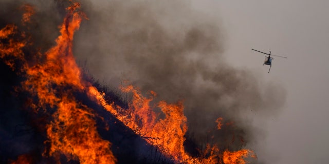 A helicopter flies away after dropping water over the Blue Ridge Fire burning along the 71 state highway Tuesday, Oct. 27, 2020, in Chino Hills, Calif.
