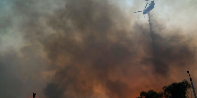 Herman Termeer, bottom left, takes pictures as a helicopter drops water over the Blue Ridge Fire burning along the hillside Tuesday, Oct. 27, 2020, in Chino Hills, Calif.