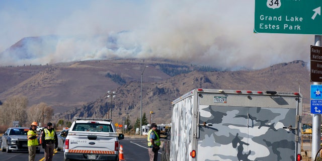 A Colorado State Patrol trooper turns away a motorist with a trailer at a roadblock as Smoke rises from mountain ridges as a wildfire burns, Thursday, Oct. 22, 2020, near Granby, Colo.