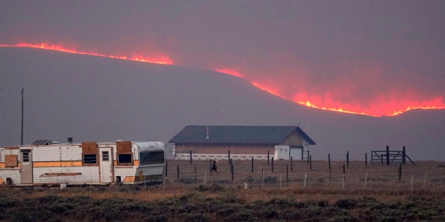 Flames rise from mountain ridges near a farmstead as the East Troublesome Fire burns near Granby, Colo.