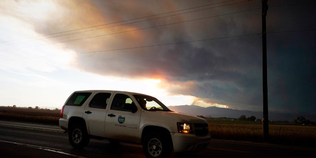 Smoke rises from mountain ridges as several wildfires burn in the state Wednesday, Oct. 21, 2020, as traffic moves along 75th street in Niwot, Colo.