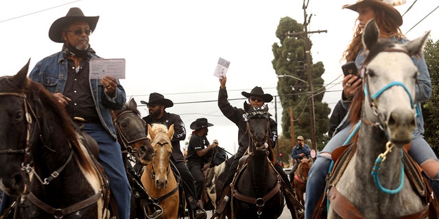 Compton Cowboys, some lifting their ballots, ride through the streets of Compton toward the Compton Library to cast their votes in a ballot box on October 25, 2020. (Photo by Genaro Molina/Los Angeles Times via Getty Images)