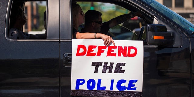 A protester holds a sign that says "Defend the Police" as pro-police protesters pass through downtown Bloomington, Indiana, during a "Defend the Police" event in support of the police and to protest against defunding the police Aug. 8, 2020.