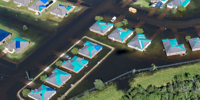 Water surrounds houses with tarps in the aftermath of Hurricane Delta, Saturday Oct. 10, 2020, in Iowa, La.