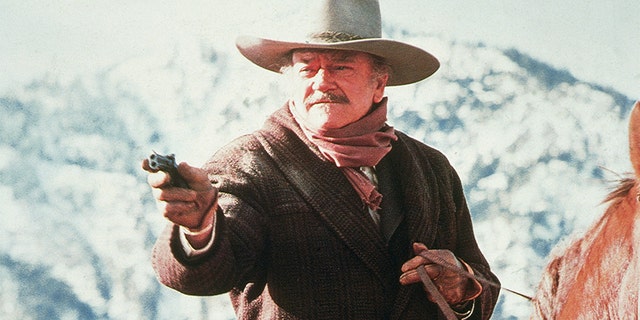 L'attore americano John Wayne (1907 - 1979) punta una pistola mentre cavalca in una scena di 'The Shootist,' 1976. 'The Shootist,'la storia di un pistolero morente che vive i suoi ultimi giorni, è stato l'ultimo film di Wayne.
