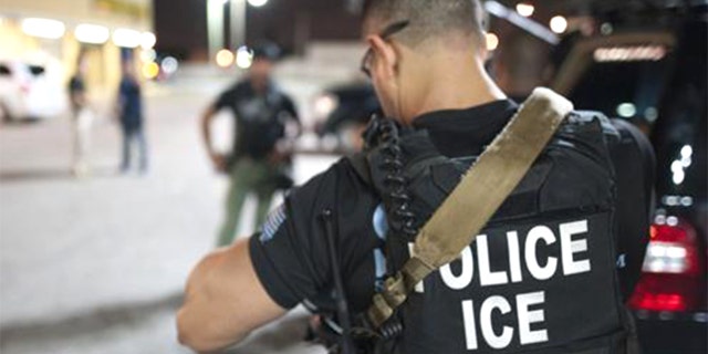 An Immigrations and Customs Enforcement officer preparing for an arrest in a parking lot.