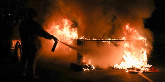 A person uses a fire extinguisher to put out a burning barricade in Philadelphia on October 27, 2020, during a protest over the police shooting of 27-year-old Walter Wallace. (Photo by Gabriella AUDI / AFP) (Photo by GABRIELLA AUDI/AFP via Getty Images)