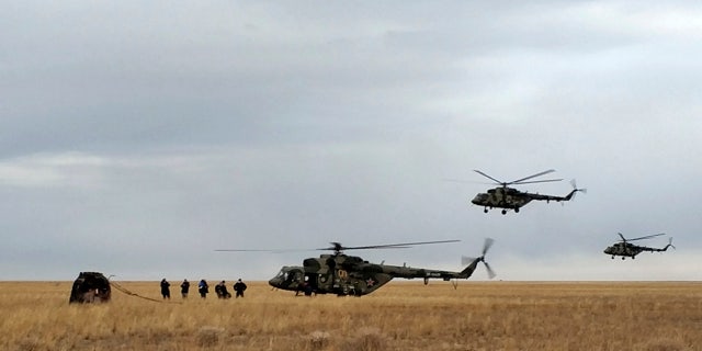 In this photo released by Rosaviatsiya, Russian rescue team helicopters land near a Russian Soyuz MS-16 capsule, left, landed near town of Dzhezkazgan, Kazakhstan, Thursday, Oct. 22, 2020. Rosaviatsiya via AP