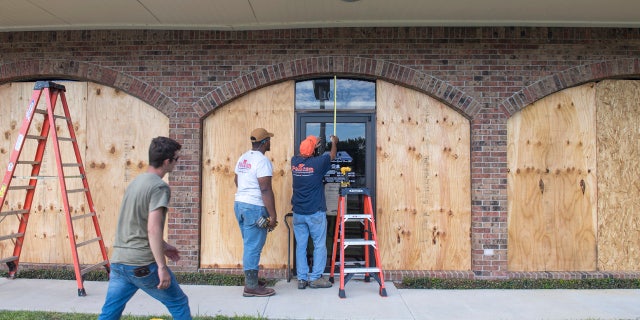 Bernie Arnould, center, gets help from Kaden Ashley and D.J. Hebert, left, all with Pelican Companies, as they board up the windows to the front of MC Bank in Amelia, La., Wednesday, Oct., 7, 2020, in In preparation for Hurricane Delta.