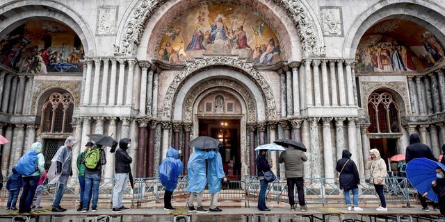 Visitors stand on on a trestle bridges as they admire St. Mark's Basilica during an expected high water, in Venice, northern Italy, Saturday, Oct. 3, 2020.