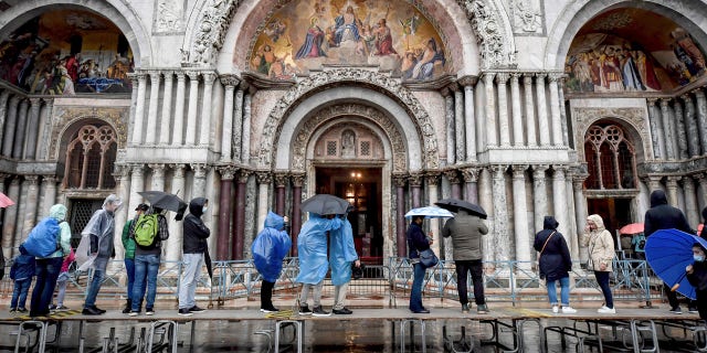 Visitors stand on on a trestle bridges as they admire St. Mark's Basilica during an expected high water, in Venice, northern Italy, Saturday, Oct. 3, 2020.