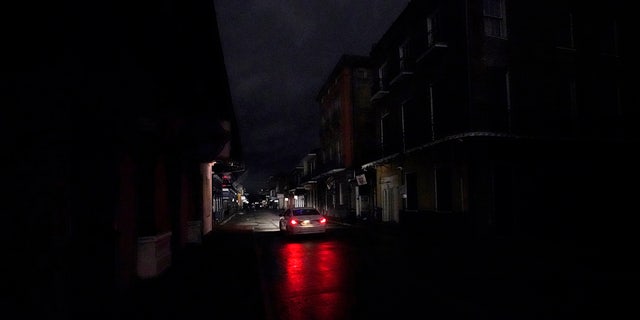 A passing car's headlights illuminate a darkened Bourbon Street in the French Quarter of New Orleans, Wednesday, Oct. 28, 2020.