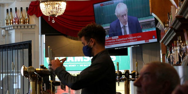 A member of staff pours a drink in the Richmond pub as the TV screen shows Britain's Prime Minister Boris Johnson delivering a statement from the House of Commons, in Liverpool, England, Monday, Oct. 12, 2020. (Peter Byrne/PA via AP)