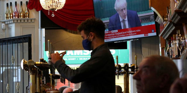 A member of staff pours a drink in the Richmond pub as the TV screen shows Britain's Prime Minister Boris Johnson delivering a statement from the House of Commons, in Liverpool, England, Monday, Oct. 12, 2020. (Peter Byrne/PA via AP)